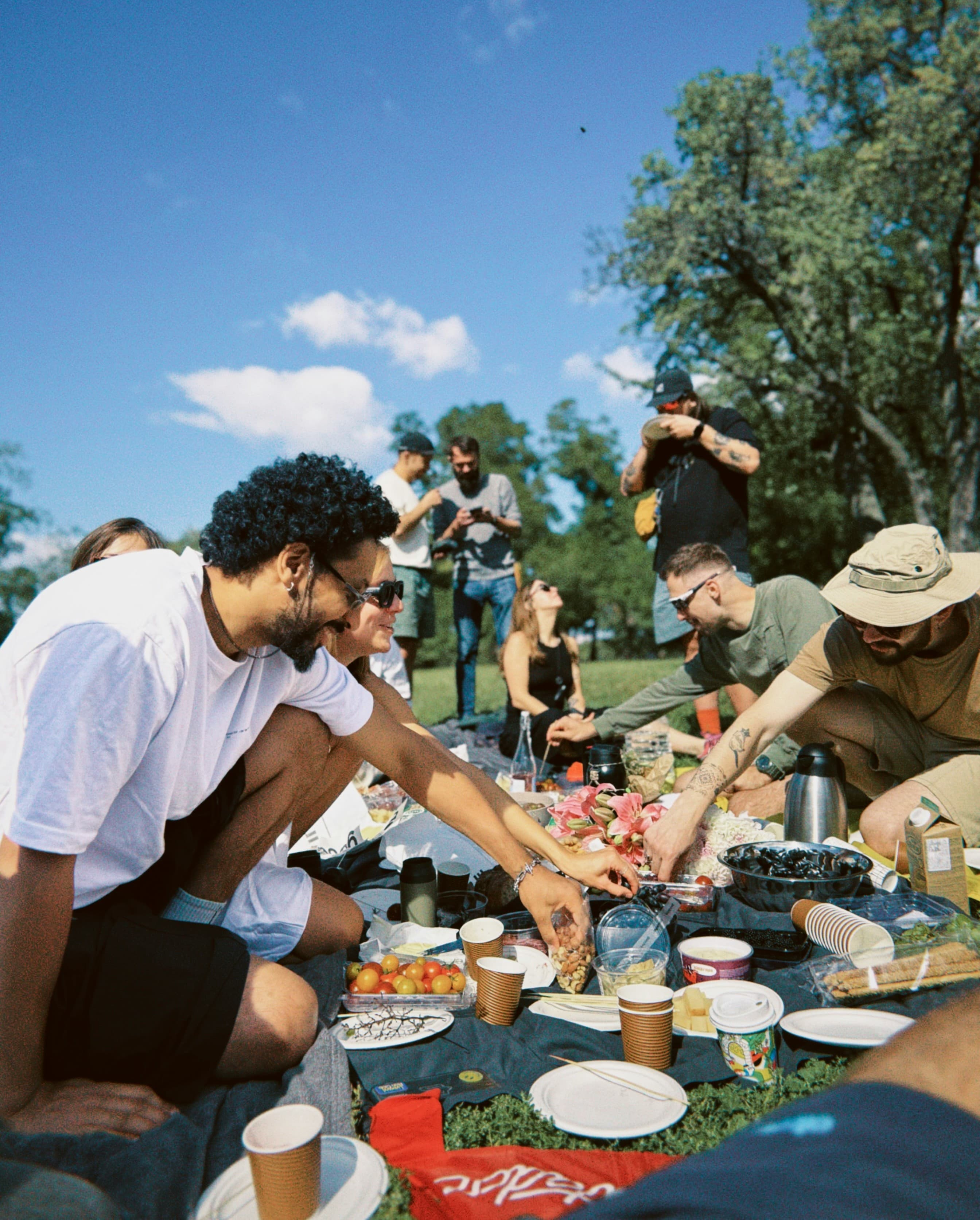 A group of people sitting on blankets in a park on a sunny day, sharing food and drinks