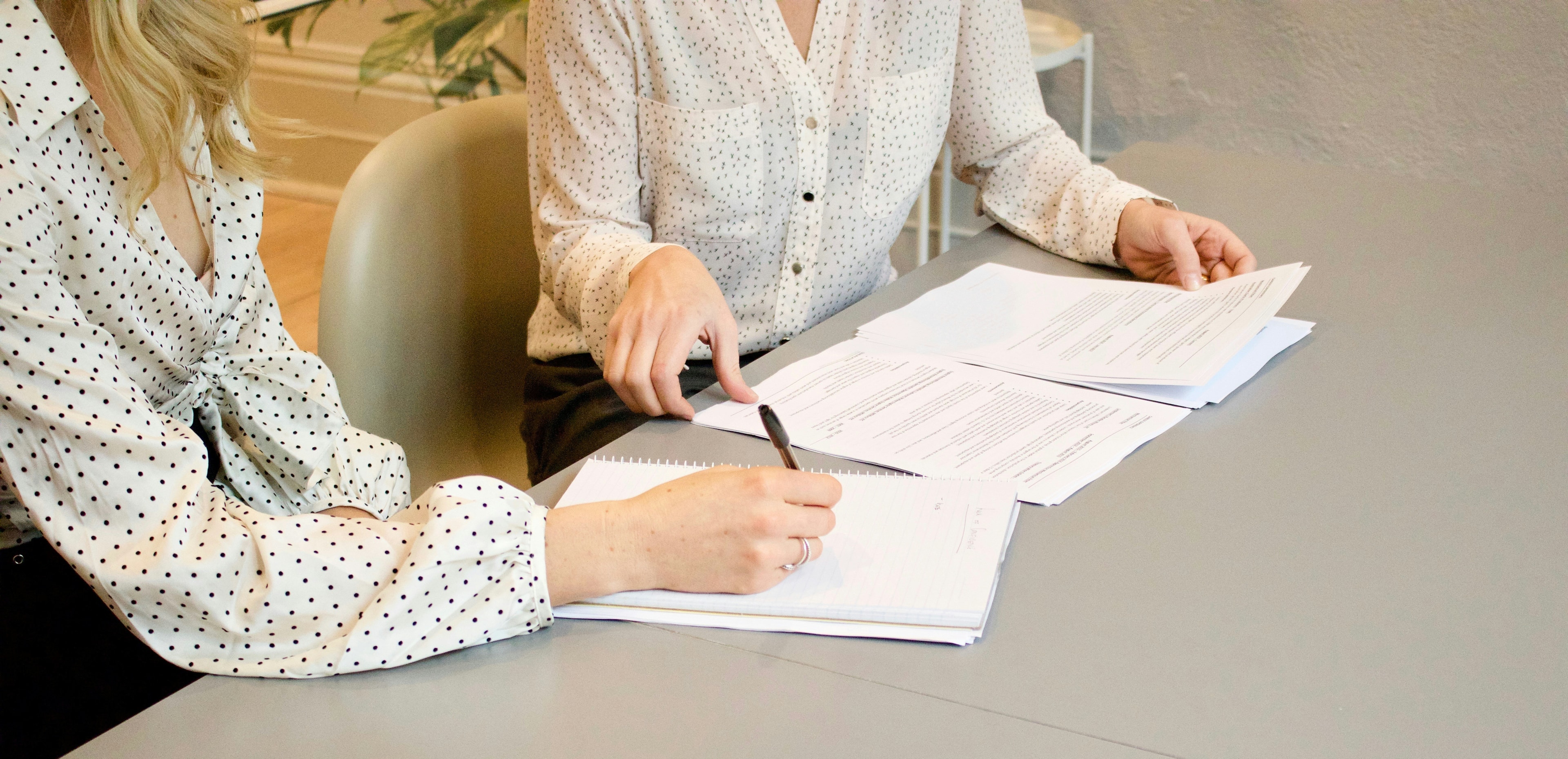 Two people at a table reviewing papers, one writing in a notebook